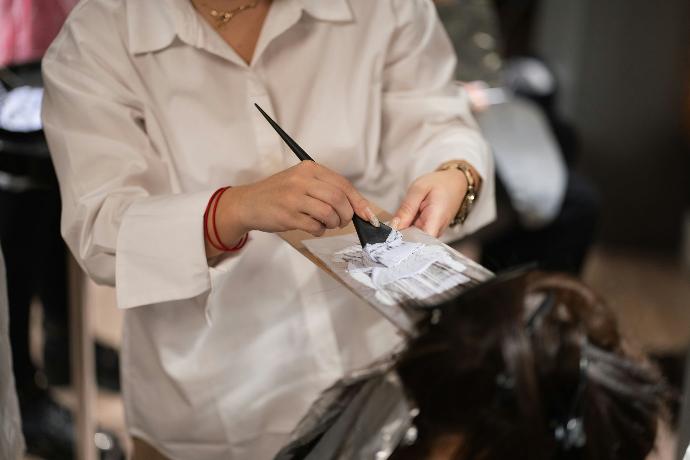 Femme avec une chemise blanche qui applique une coloration au pinceau sur des cheveux bruns