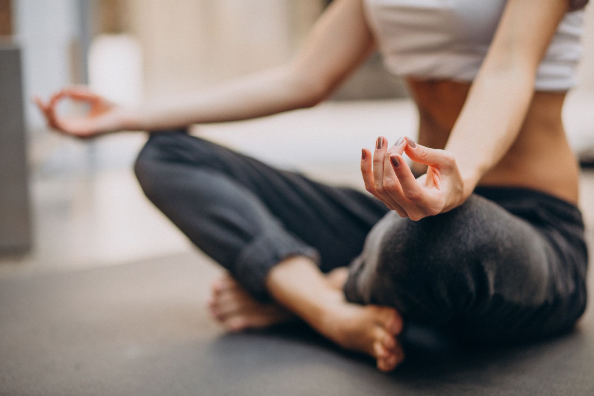 femme assise en tailleur avec un tee-shirt blanc et un jogging gris qui fait du yoga