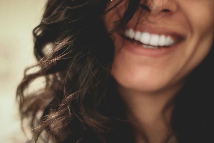 Gros plan d'une femme brune aux cheveux longs et ondulés dont on voit juste le sourire