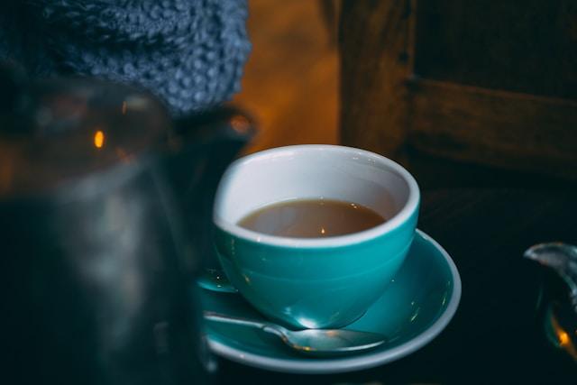 tasse de thé et soucoupe bleu turquoise avec une petite cuillère et au premier plan bouilloire noire