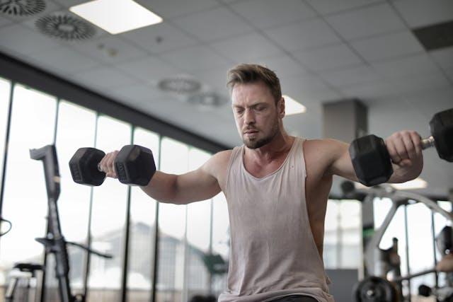 Homme en débardeur blanc dans une salle de sport qui soulève des poids