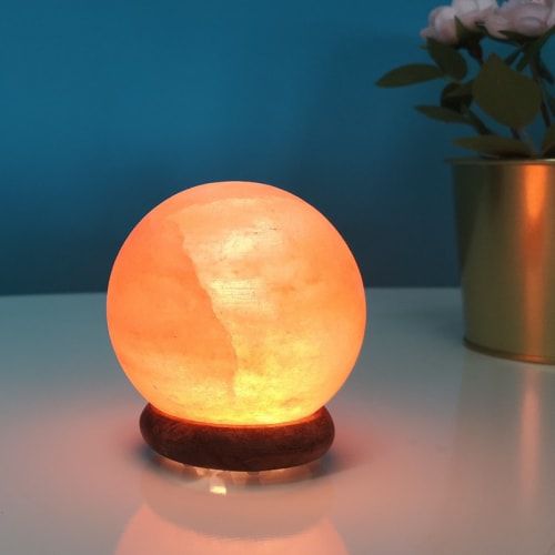 Lampe en cristal de sel ronde allumée avec plante en pot en arrière-plan