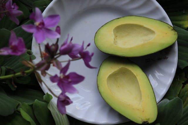 Deux moitiés d'avocat dans assiette blanche avec au premier plan des fleurs violettes