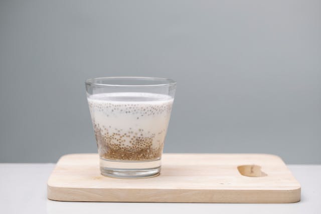Glass with milk and chia seeds on a light wood plinth with grey background