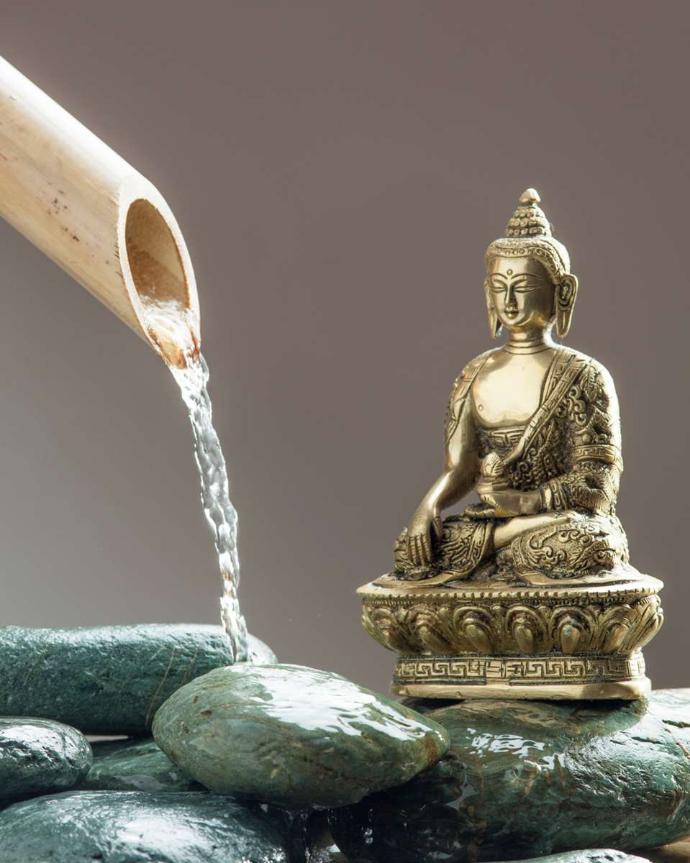 Buddha aus vergoldetem Metall auf nassen Steinen mit Bambusrohr, aus dem Wasser kommt
