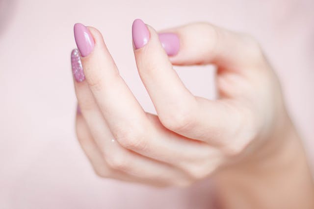 Ongles de femme avec vernis rose dont un pailleté