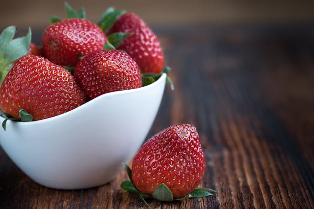 Fraises dans un ramequin blanc avec une fraise à côté posée sur une table en bois foncée