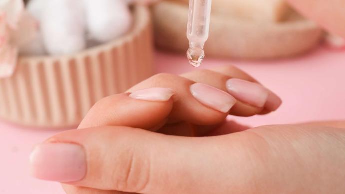 Main de femme avec ongles rose pâle et pipette d'huile au-dessus d'un ongle
