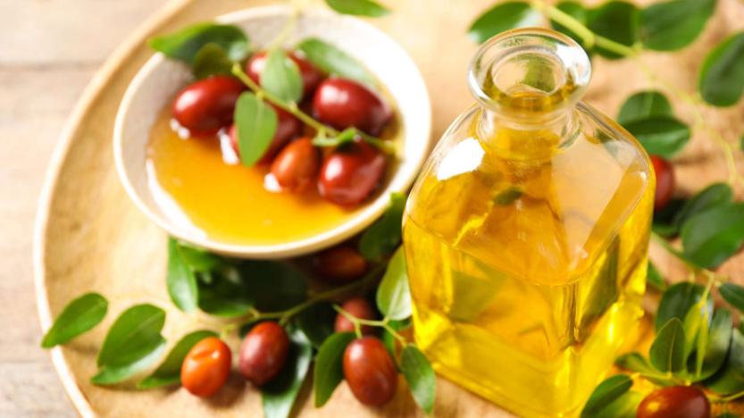 Flacon d'huile végétale avec des graines de jojoba et des feuilles autour 