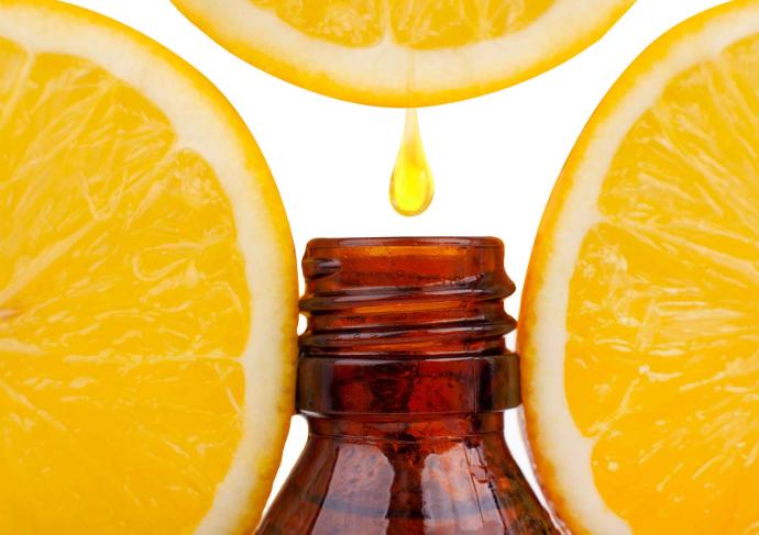 Rondelles de citron entourant un flacon d'huile essentielle avec goutte qui tombe dedans