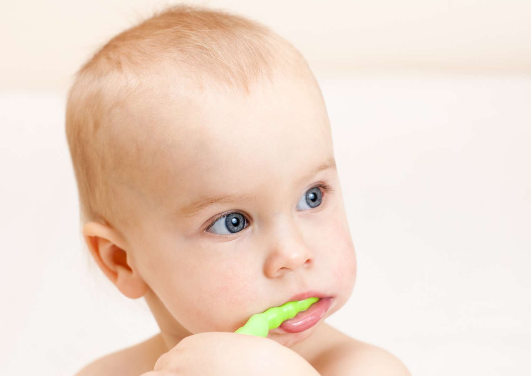Bébé blond aux yeux bleus avec une brosse à dents verte dans la bouche qu'il tient d'une main