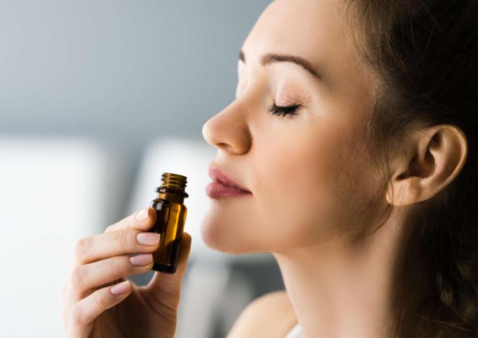 Femme de profil les yeux fermés qui respire au-dessus d'un flacon d'huile essentielle qu'elle tient à la main