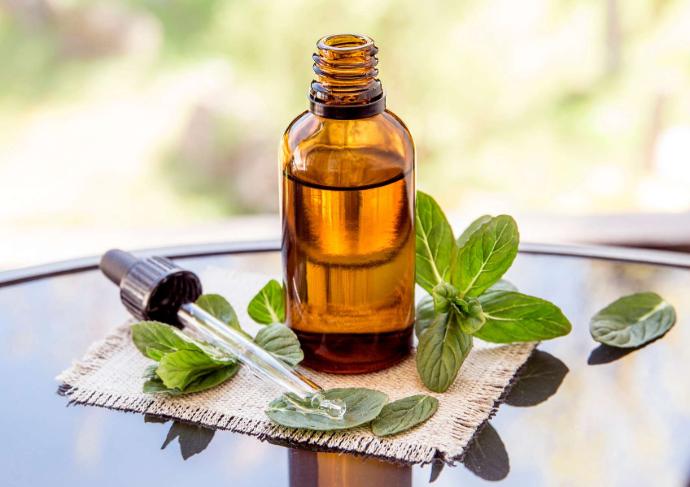 Flacon marron d'huile essentielle sur une table en verre avec à côté pipette et feuilles de menthe