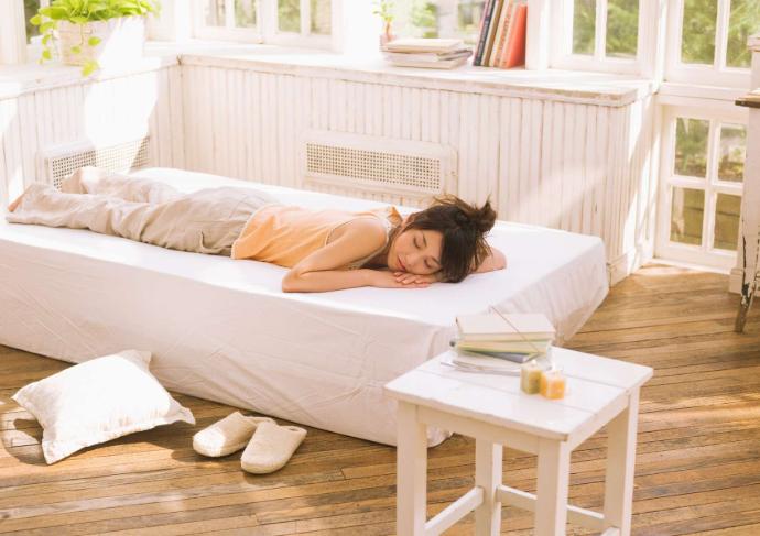 Femme allongée sur le ventre sur un lit blanc qui fait la sieste avec une table basse posée à côté