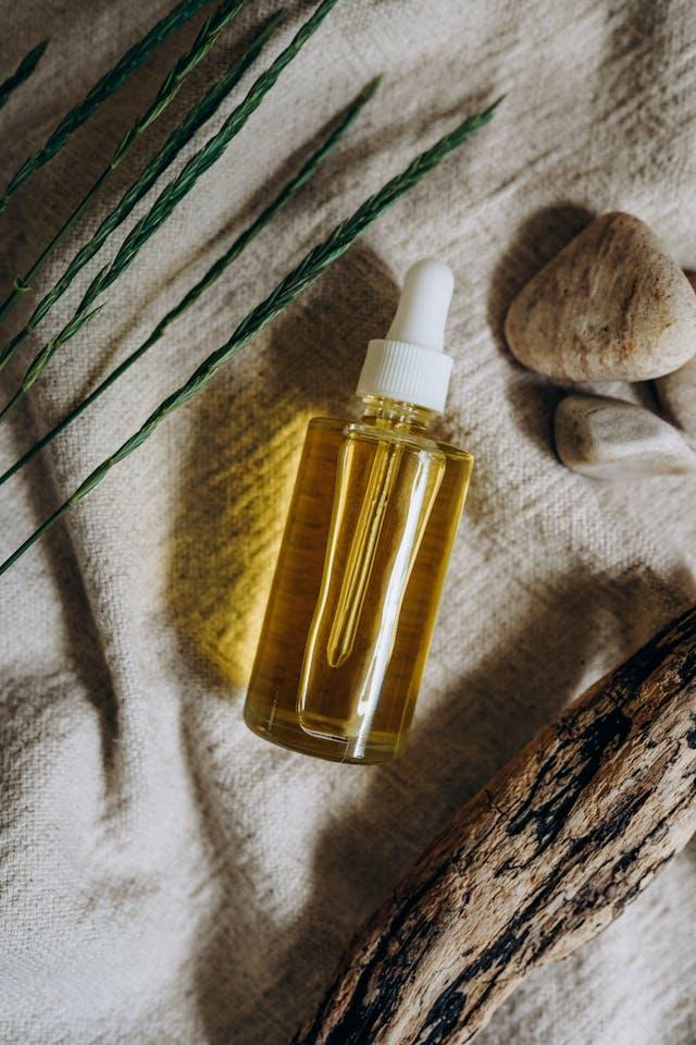 Flacon d'huile cosmétique posé sur tissu beige avec feuilles, cailloux et bois flotté
