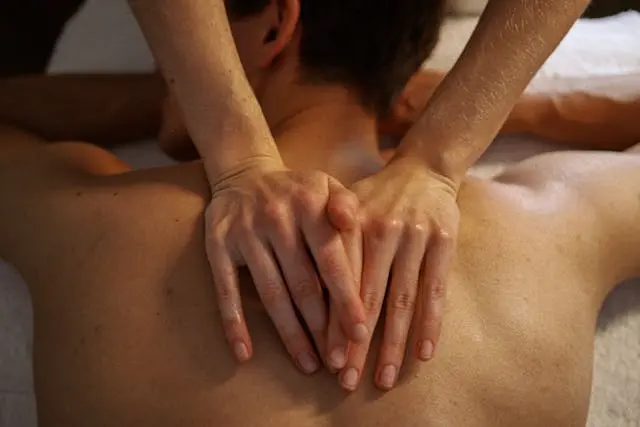 Mains de femme vues de haut qui massent un dos d'homme allongé sur le ventre sur une serviette blanche