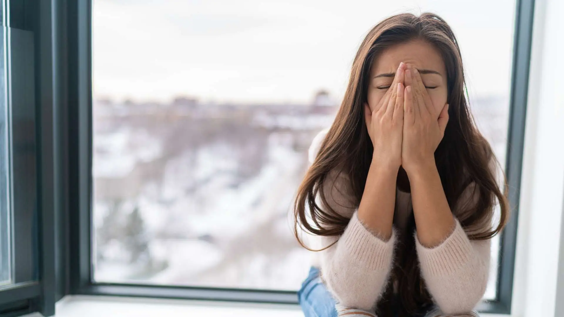 Jeune femme brune cheveux longs  le visage dans les mains dos à une fenêtre