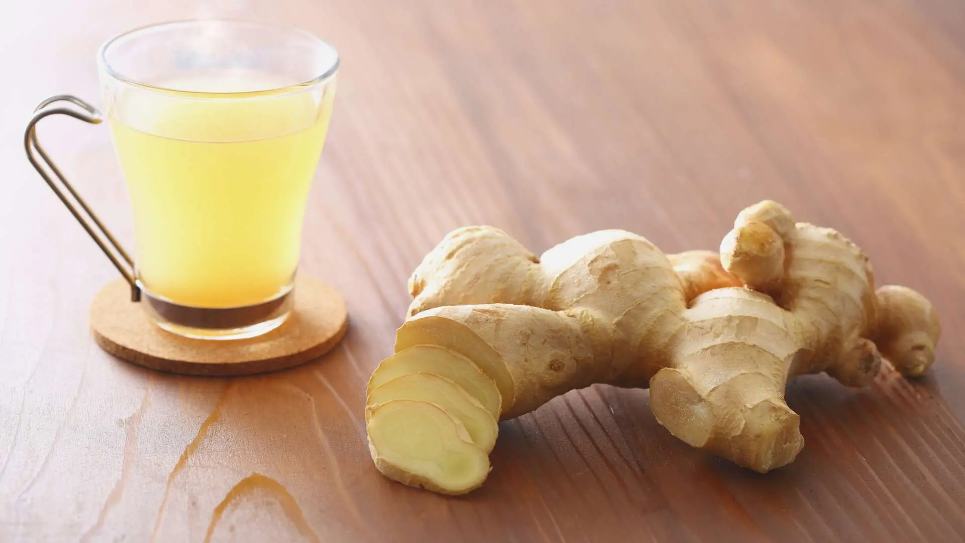 Tasse avec infusion de gingembre et racines de gingembre à côté posés sur une table en bois