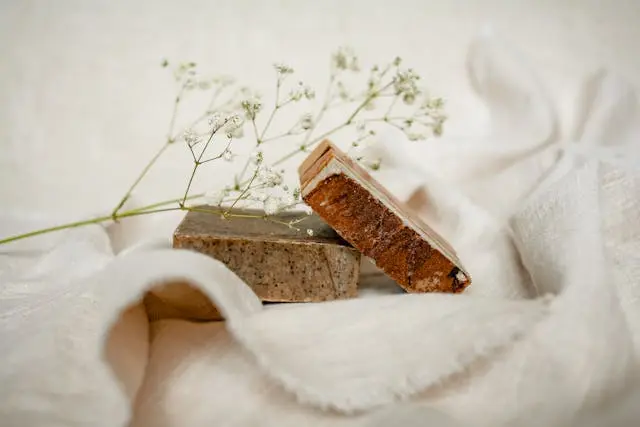 Deuxa savons artisanaux marrons posés sur tissu en lin blanc avec une branche de gypsophile 